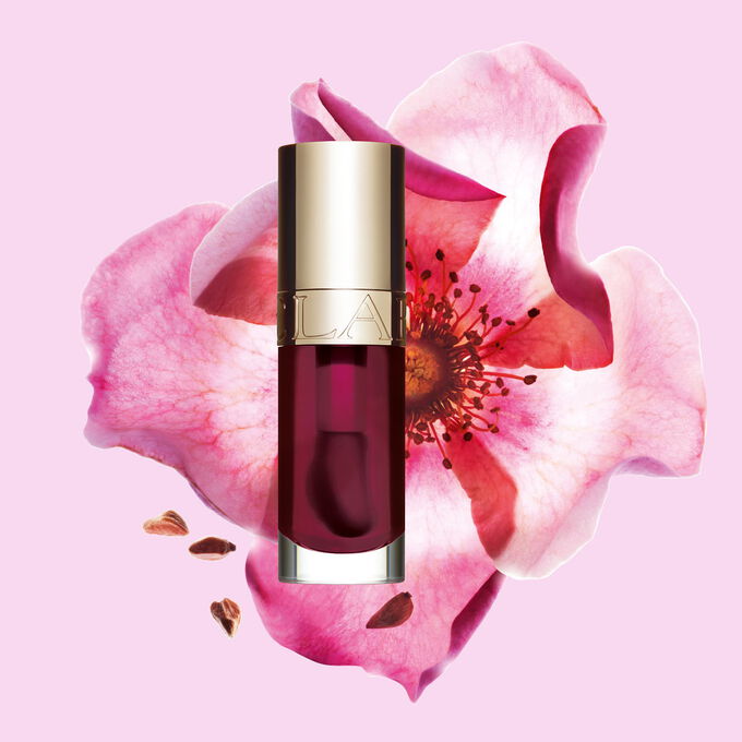 Packshot of Clarins Lip Comfort Oil Fig, placed next to a sweetbriar rose on a light pink background.