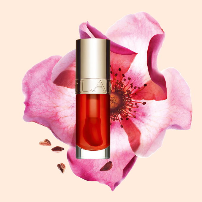 Packshot of Clarins Lip Comfort Oil Apricot, placed next to a sweetbriar rose on a light orange peach background.