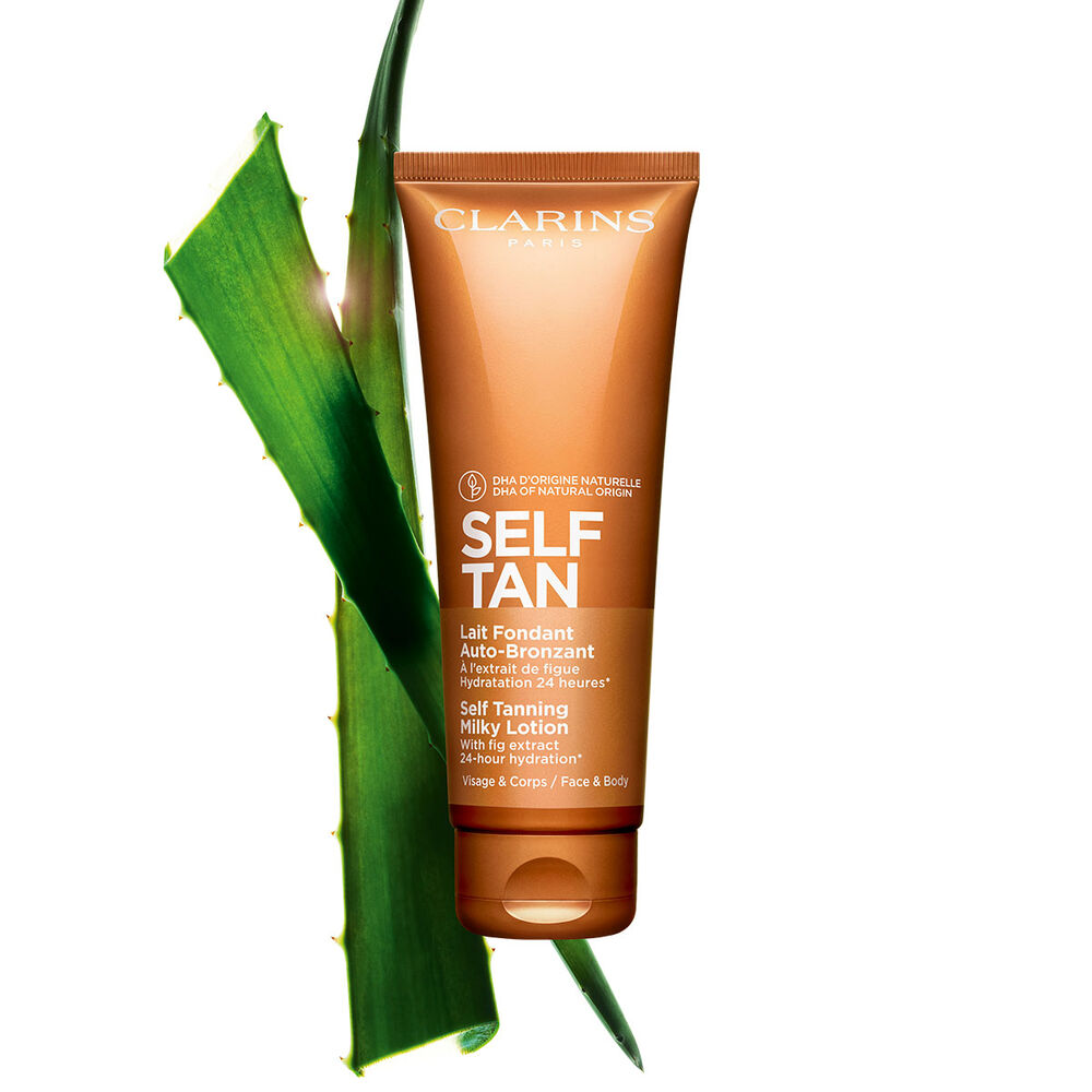 Packshot of a tube of Clarins Self Tanning Milky Lotion close to a piece of aloe vera on a pale orange background.