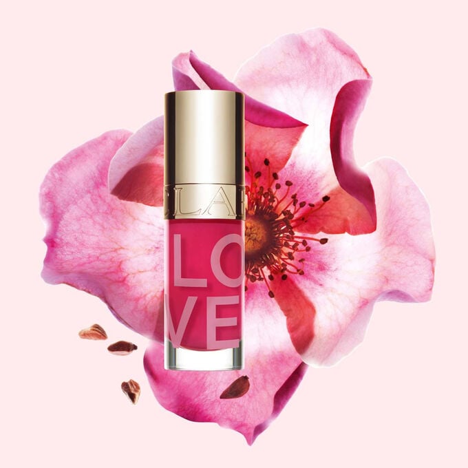 Packshot of Lip Oil Limited Edition Love Collection in front of a rose on a light pink background emphasizing its vibrant color