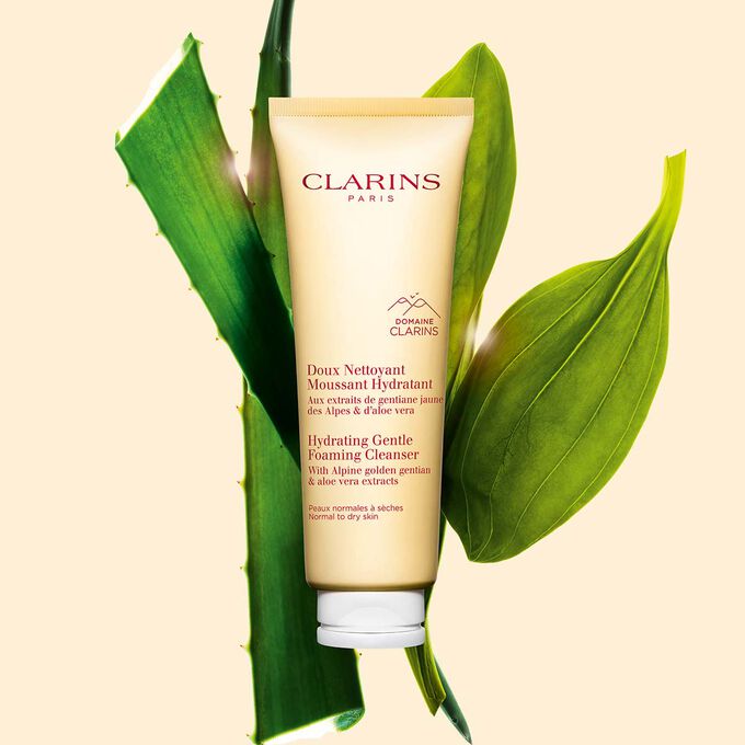 Packshot of the hydrating gentle foaming cleanser yellow tube next to golden gentian and aloe vera on light yellow background