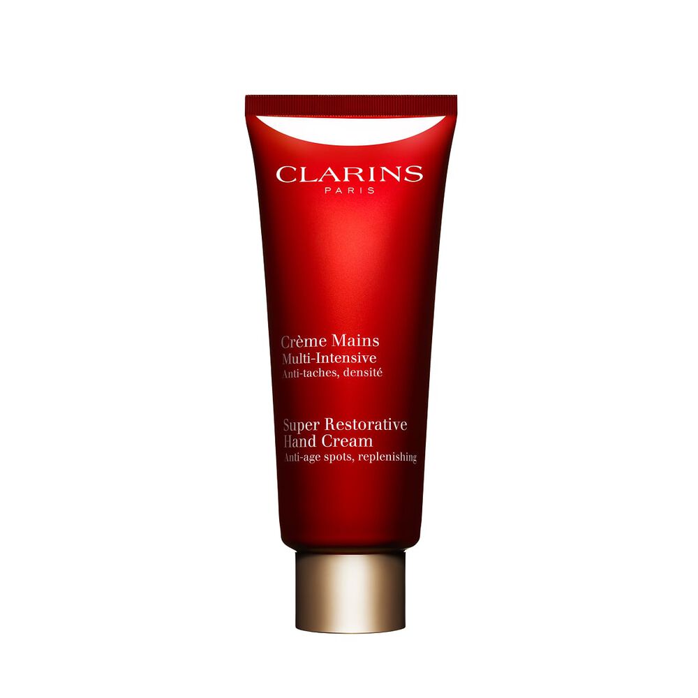 Packshot of a bottle of Clarins Super Restorative Hand Cream close to some harungana leafs on a pink background.
