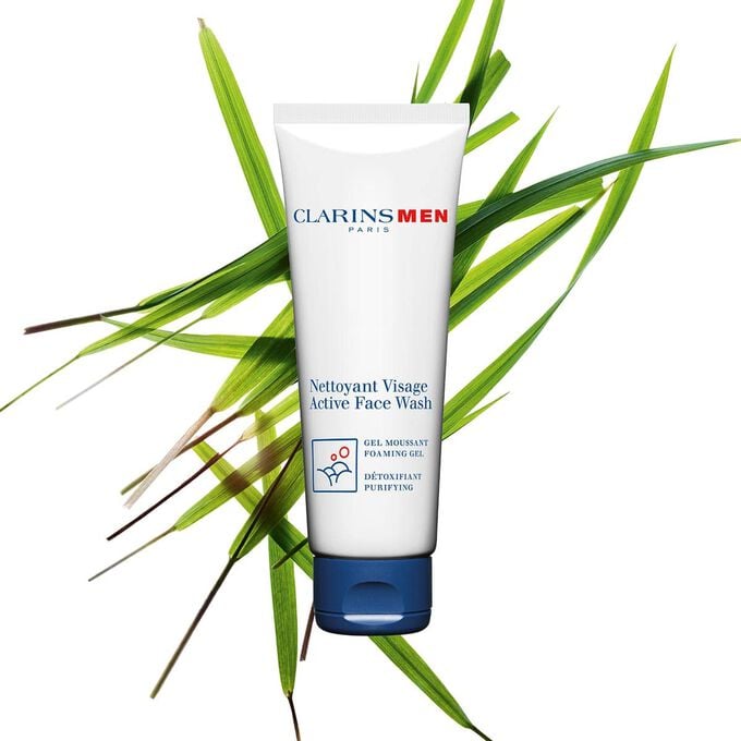Packshot of the Active Face Wash, men's face cleanser by Clarins next to bison grass to emphasize its key ingredient.