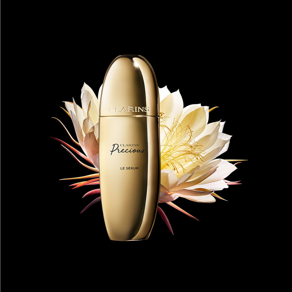 Packshot of Clarins Precious Serum close to a Moonlight flower on a dark background.