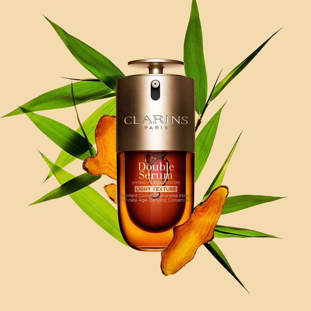 A 30ml bottle of Clarins Double Serum Light Texture among turmeric and provençal reed leaves against an orange background.