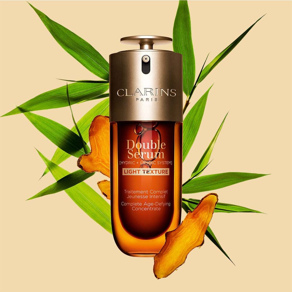 A 50ml bottle of Clarins Double Serum Light Texture among turmeric and provençal reed leaves against an orange background.