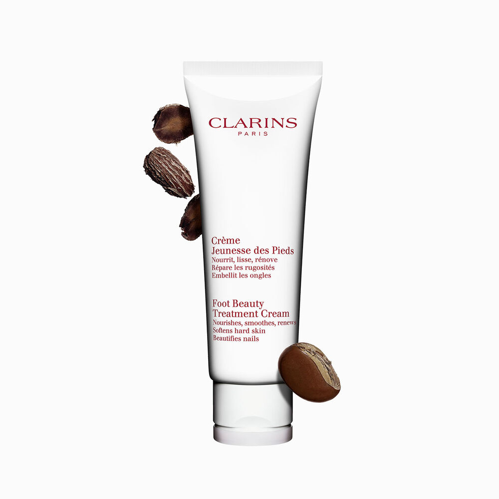 Packshot of a bottle of Clarins Foot Beauty Treatment Cream close to some shea nuts on a white background.