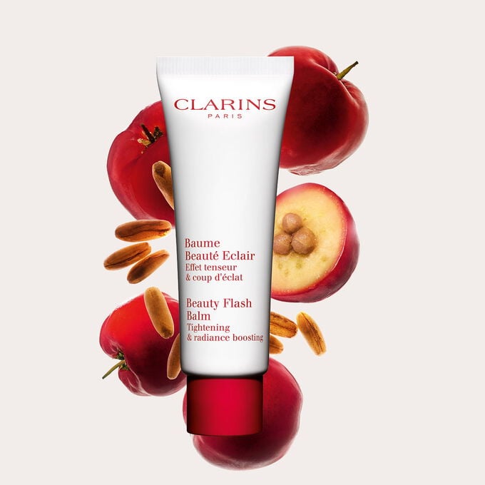Packshot of a tube of Clarins Beauty Flash Balm close to acerola berries on a peach background.