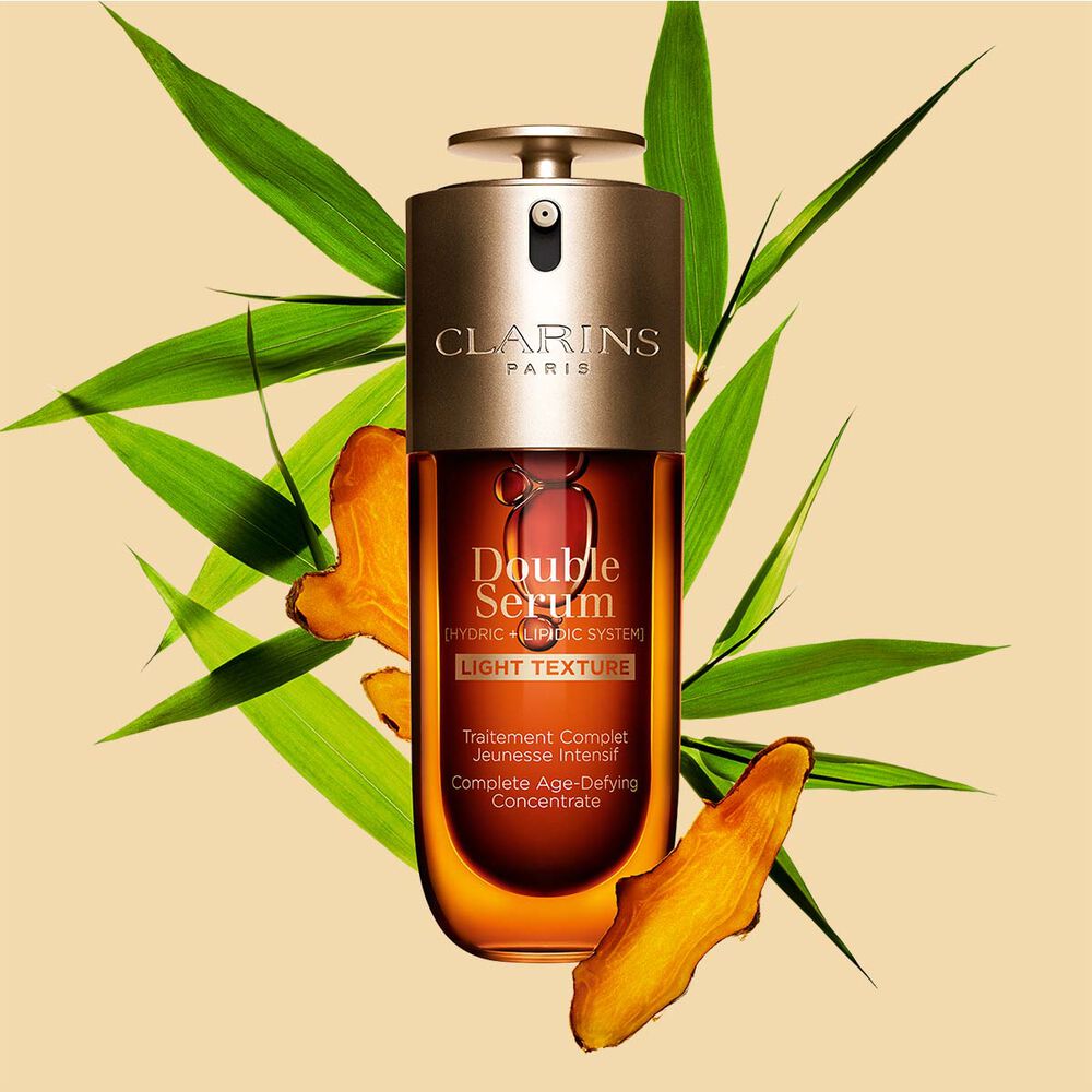 A 70ml bottle of Clarins Double Serum Light Texture among turmeric and provençal reed leaves against an orange background.