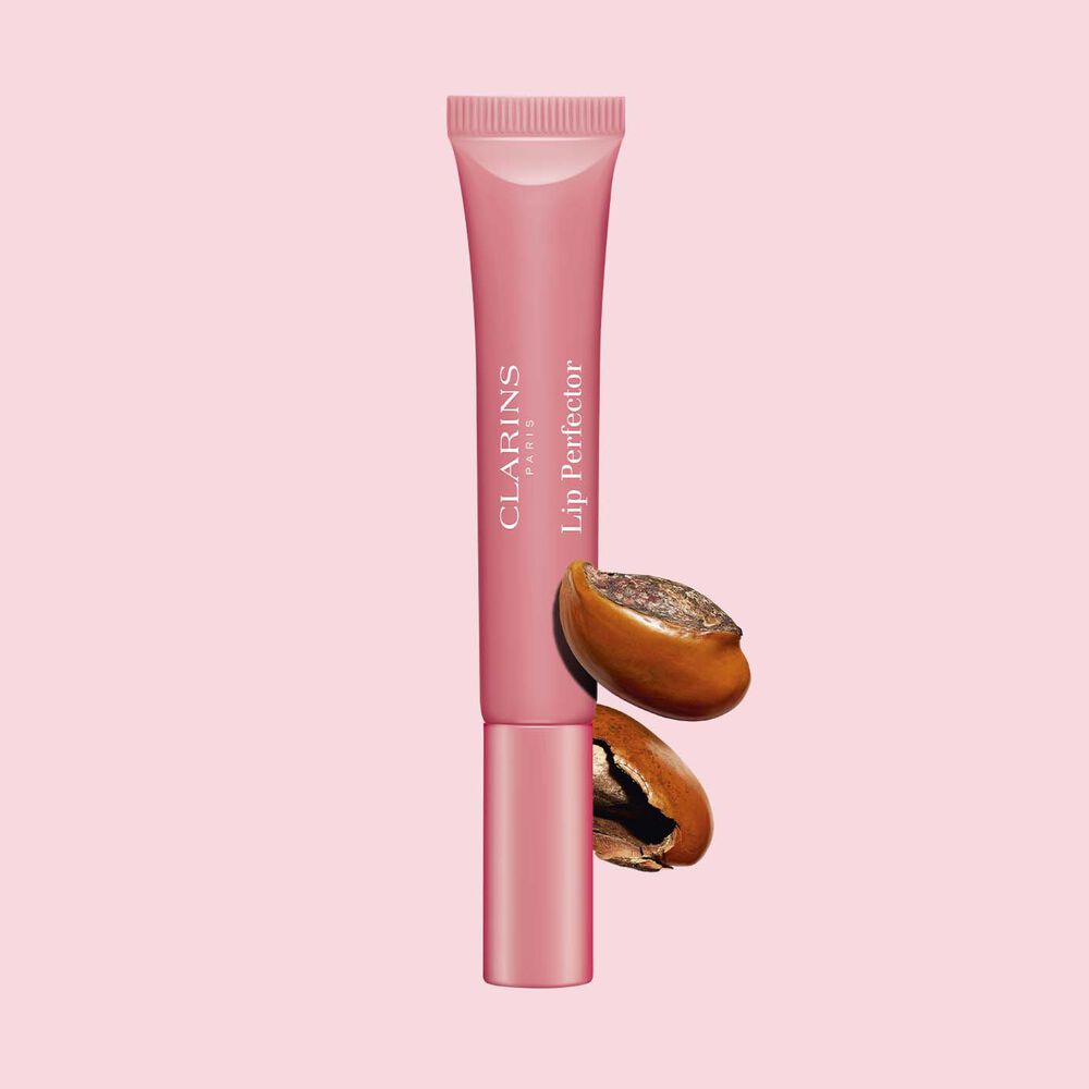 Packshot of Clarins Lip Perfector 01 Rose Shimmer repairing lip balm in front of a shia seeds on a pink background.