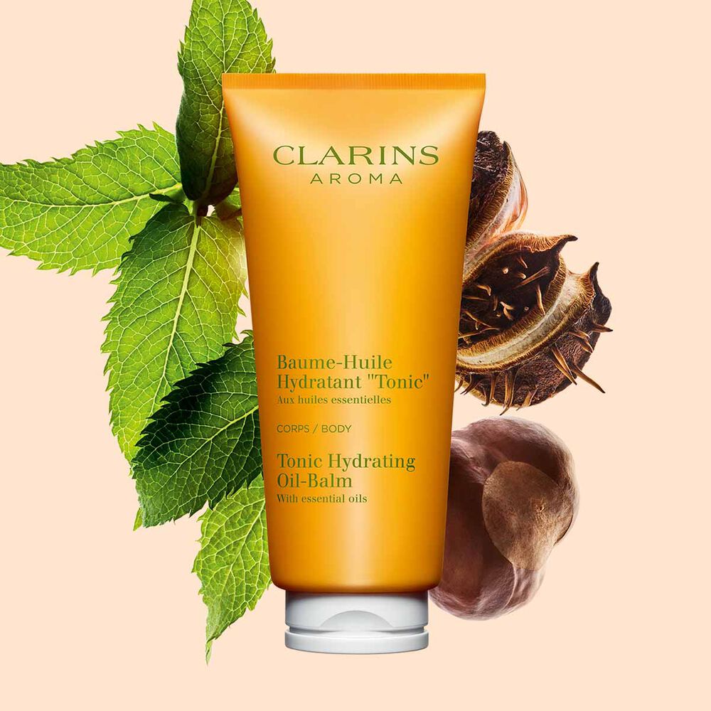 Packshot of a tube of Clarins Tonic Hydrating Oil-balm, close to some mint leaves and shea seeds on a peach background.