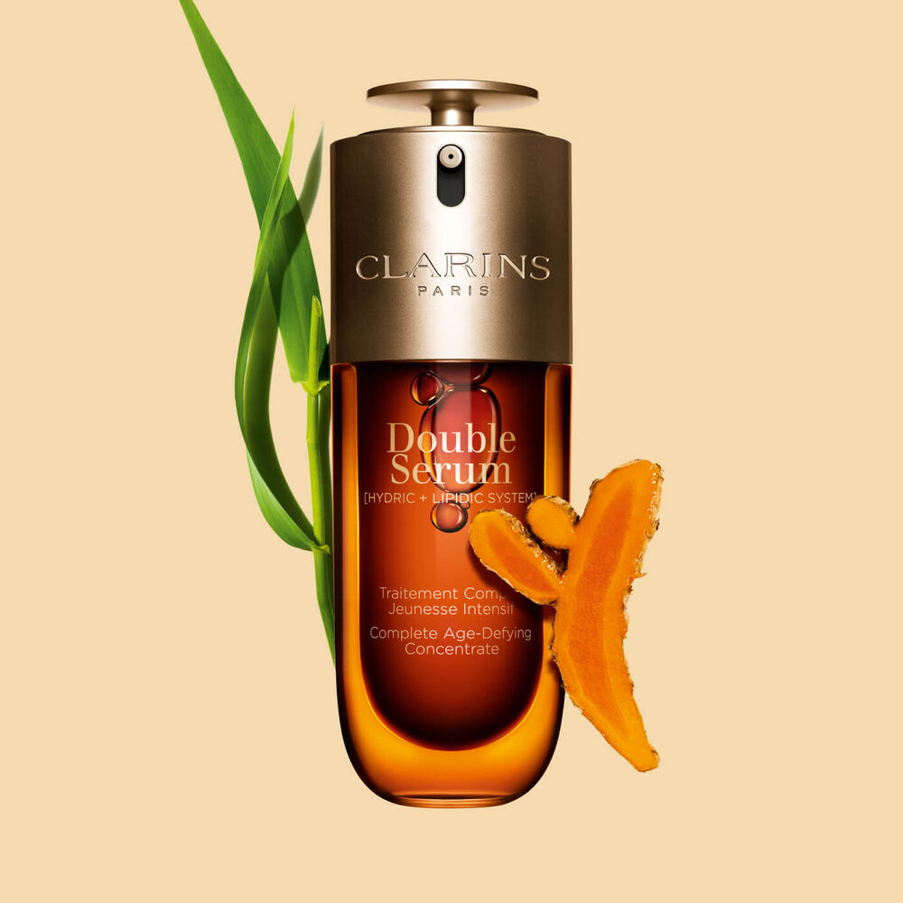 Packshot of the Clarins Double Serum displayed in front of its ingredient, including curcuma, on a gold background