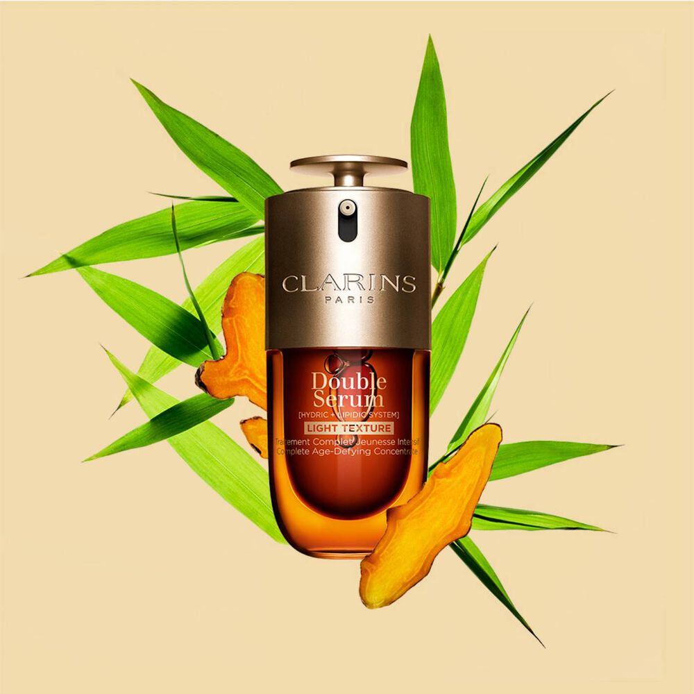 A 30ml bottle of Clarins Double Serum Light Texture among turmeric and provençal reed leaves against an orange background.