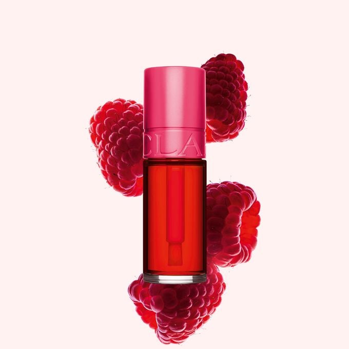 Packshot of Clarins Fushia Water Lip Stain in shade 01, placed beside rasberries on a light pink background.