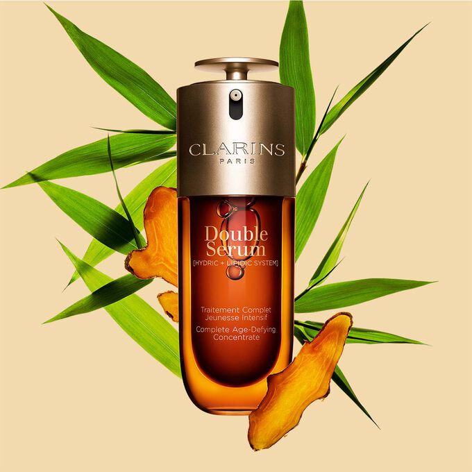 Packshot of the Clarins Double Serum displayed in front of its ingredient, including curcuma, on a gold background
