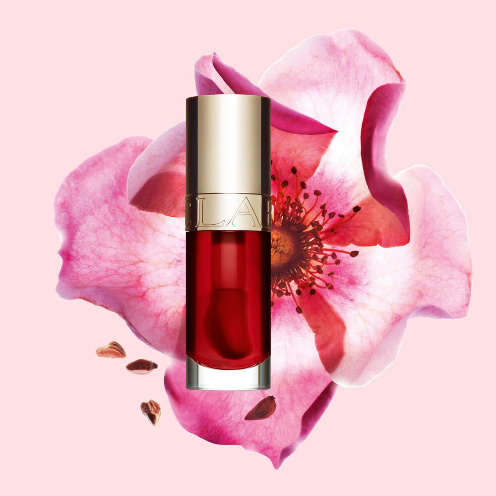 Packshot of Clarins Lip Comfort Oil Strawberry, placed next to a sweetbriar rose on a light pink background.