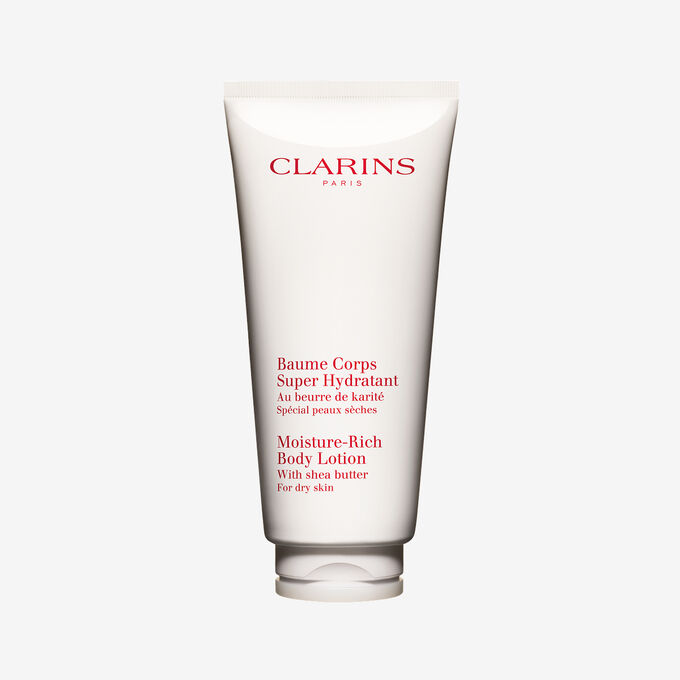 Clarins moisture rich body lotion tube displayed with natural shea butter shells on an elegant white backdrop.
