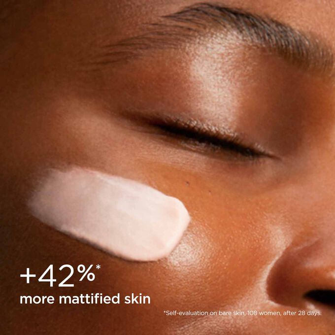 Woman with closed eyes, wearing SOS Primer Mattifying by Clarins on her face to illustrate that it reduces skin shine by 39%.