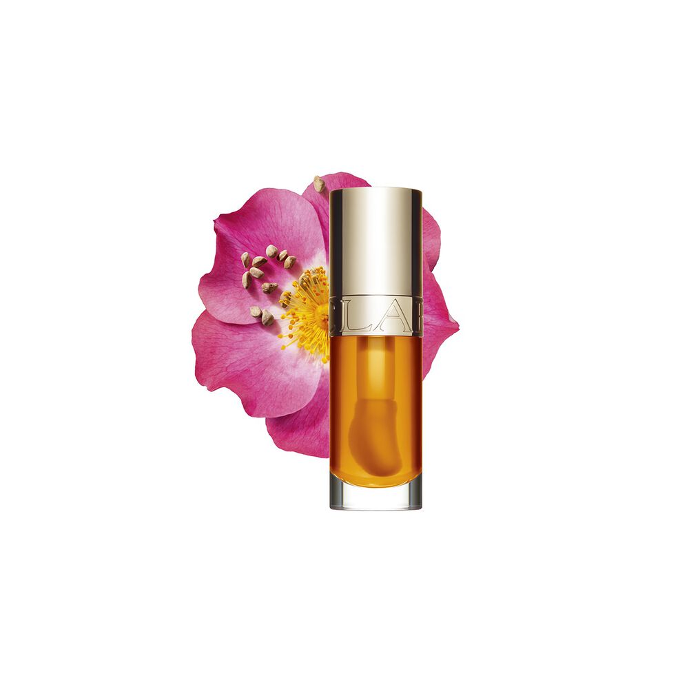 Packshot of Clarins Lip Comfort Oil in Honey, placed next to a sweetbriar rose on a light peach background.