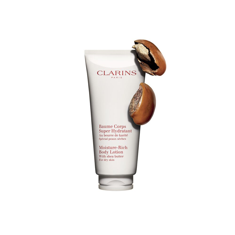Packshot of a tube of Clarins Moisture-Rich Body Lotion by Clarins close to some shea nuts on a white background.