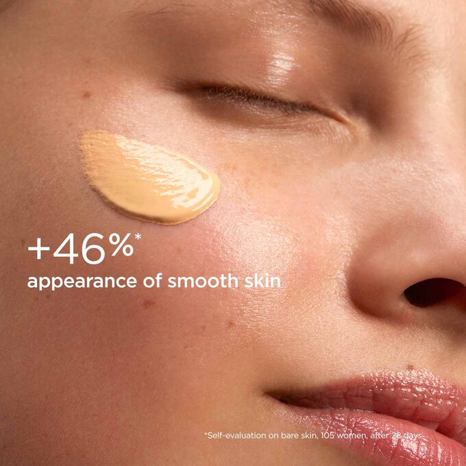 Woman with closed eyes, wearing SOS Primer Peach by Clarins on her face to illustrate that it reduces dark spots by 25%.